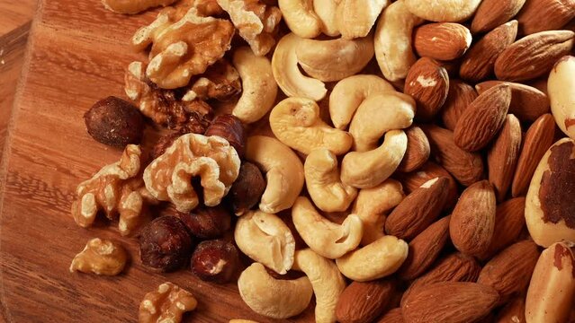 Mix with different types of nuts on a wooden plate. Nuts, cashews, almonds and Brazilian nuts. Close up healthy food with proteins. Top view great texture background, 4k video.