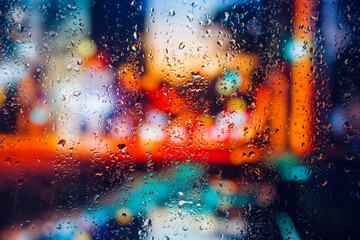 City view through a window on a rainy night,Rain drops on window with road light bokeh, City life in night in rainy season abstract background. Focus on drops on glass