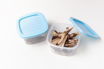 Dried mushrooms in plastic containers on white background. Storage of dried mushrooms. Containers with blue lids