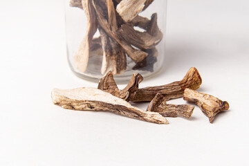 Dried mushrooms in glass jar and scattered nearby on white background. Storage of dried mushrooms