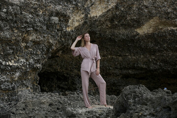 Portrait of beautiful young woman in beige silk outfit on wild rocky beach