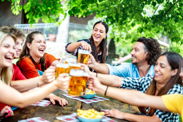 Young friends drinking and toasting beer at brewery bar restaurant - Beverage life style concept with happy guy and girls having fun together out side - Bright vivid filter with focus on mid woman
