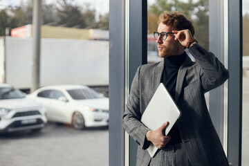 Handsome male entrepreneur in stylish formal business suit, looks through window in office interior