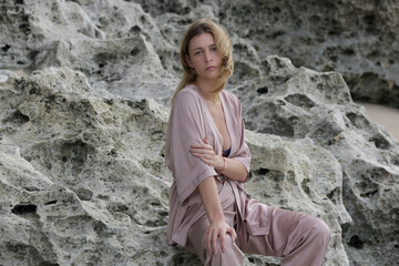 Naklejka na ściany i meble Portrait of beautiful young woman in beige silk outfit on wild rocky beach