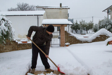 Image of a man with a shovel as he laboriously shovels snow from his driveway.
