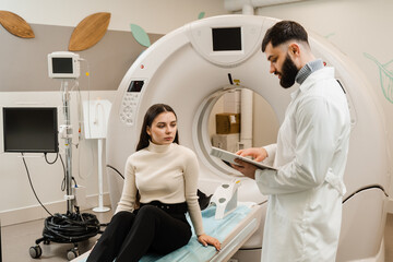 Consultation before computed tomography x-ray scan procedure to obtain detailed internal images of girls body. Doctor with woman patient in CT scanning room in medical clinic.