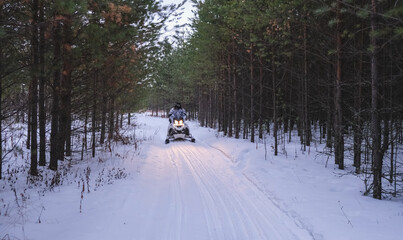 Hunters on snowmobiles ride in the winter forest