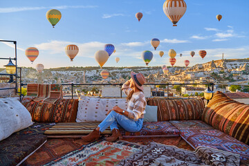 Girl traveler vacations on hotel terrace in beautiful destination in Goreme, Turkey. Fabulous Kapadokya with flying air balloons at sunrise, Anatolia