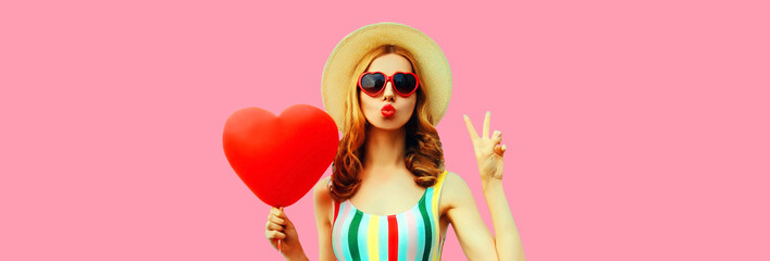 Portrait of beautiful young woman with big red heart shaped balloon blowing her lips wearing summer...