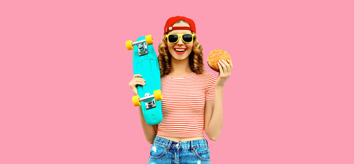 Portrait of stylish young woman with burger fast food and skateboard wearing baseball cap, sunglasses on pink background