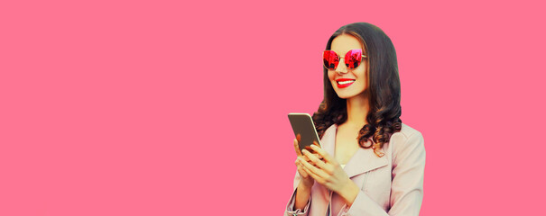 Portrait of beautiful happy smiling young woman with smartphone wearing pink sunglasses on pink...