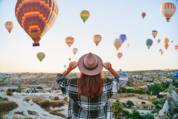 Girl traveler vacations beautiful destination in Goreme, Turkey. Fabulous Kapadokya with flying air balloons at sunrise, Anatolia - obrazy, fototapety, plakaty