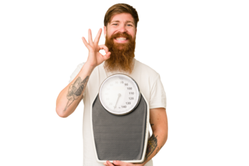 Adult redhead man with long beard holding a scale isolated cut out cheerful and confident showing ok gesture.