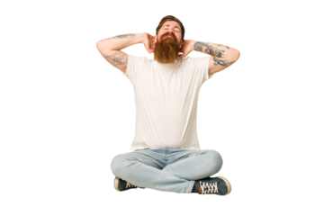 Young adult redhead with a long beard sitting on the floor isolated feeling confident, with hands behind the head.