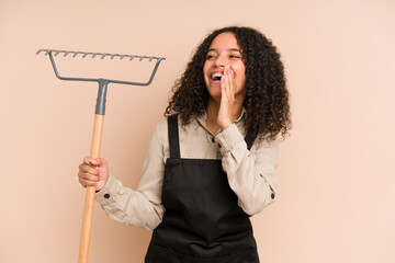 Young african american gardener woman holding a rake isolated shouting and holding palm near opened mouth.