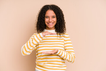 Young african american curly woman isolated holding something with both hands, product presentation.