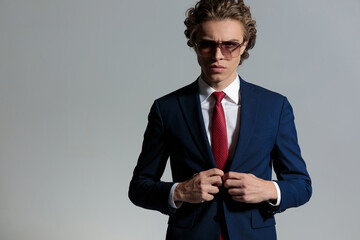 confident young businessman wearing sunglasses and unbuttoning suit