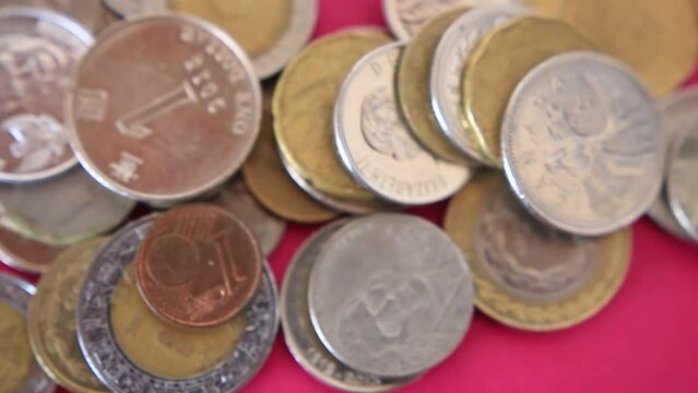 Coins from different currencies around the world are droped and staked on a  colorful pink surface 