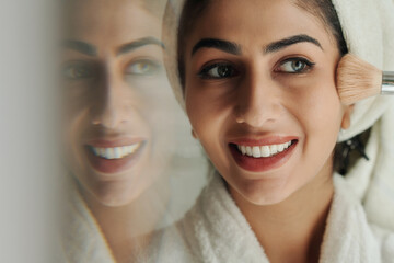Smiling young woman applying face powder when getting ready in the morning