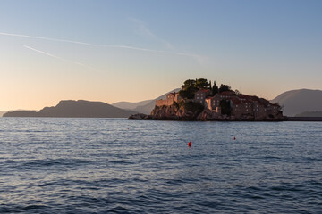 Panoramic sunset view of idyllic island Sveti Stefan in Budva Bay, Adriatic Mediterranean Sea, Montenegro, Europe. Silhouette of Dinaric Alps in back. Summer vacation in exclusive luxury seaside hotel