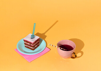 Creative party scene a piece of cake on a blue plate and a cup of red juice. Minimal concept on yellow background.