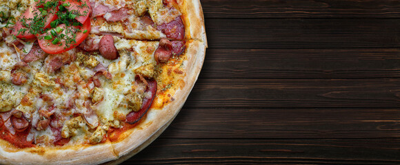 Pizza with meat sausage and chicken, cheese and tomatoes, on a wooden background