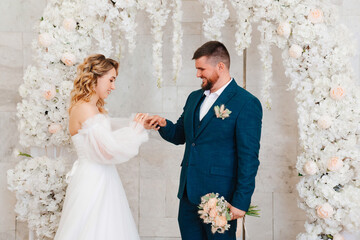 happy bride and groom exchange rings in an arch of artificial flowers.