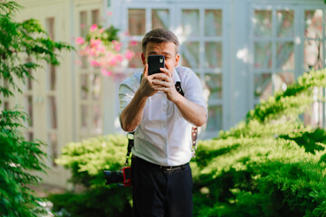 a man in a white shirt takes a photo on his smartphone in the park. 