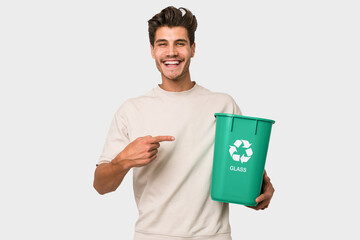 Young caucasian man holding a glass trash isolated smiling and pointing aside, showing something at blank space.