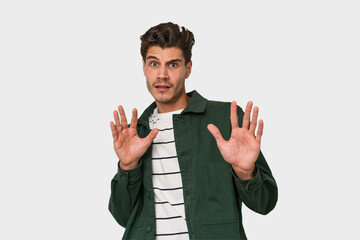 Young handsome caucasian man isolated on white background rejecting someone showing a gesture of...