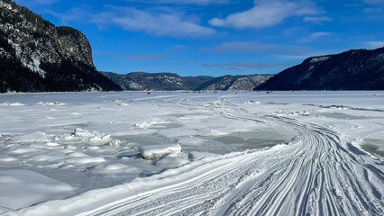 Ice fishing huts with cliffs in the background on a clear blue winter day, Eternity Bay, Saguenay Fjord, Cabada.