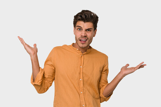 Young handsome caucasian man isolated on white background confused and doubtful shrugging shoulders to hold a copy space.