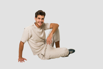 Young caucasian man sitting on the floor isolated on white background