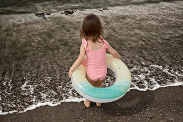 A little girl near dirty water is afraid to go for a swim because of the mud.