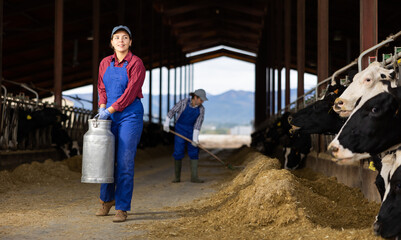 Dairy farmer woman carrying aluminum can of milk in cowshed