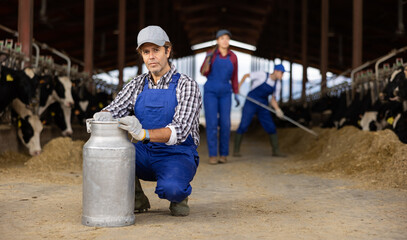 Positive man farmer standing in cowshed with arms crossed at milk can and smiling