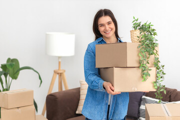 Happy young woman moving into her new home. Beautiful female student holding cardboard boxes,...