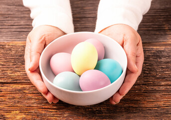 Stylish easter dyed colorful eggs on white plate, wooden rustic background, woman hands