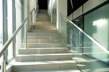 A wide staircase along the large windows in an office building. Modern interior of the lobby of an office building with large spacious windows. Illuminated long corridor in a modern business center