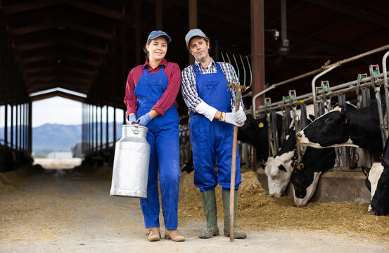 Positive Man And Woman Of Different Ages Farmers With Large Milk Can And Rake During Working Together On Dairy Farm