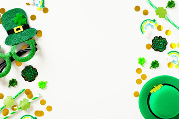 Naklejka na ściany i meble Happy St Patrick's Day background. Frame borders made of party decorations, leprechauns hats, eyeglasses, gold coins, confetti on white table. Flat lay, top view.