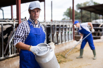 Confident farmer man holds milk can at cow farm