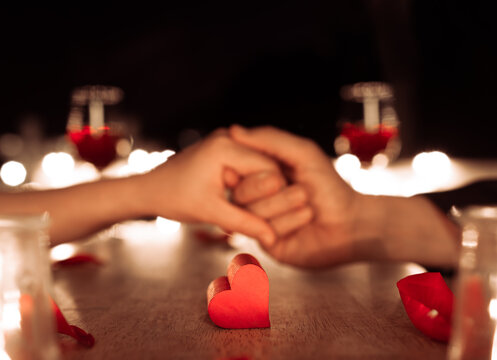 Couple holding hands in love enjoying a romantic Valentine's dinner date night. Focus on heart 