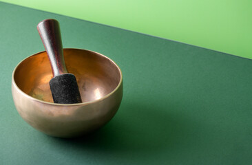 Tibetan singing bowl with sticks used during mantra meditations on green background, close up....