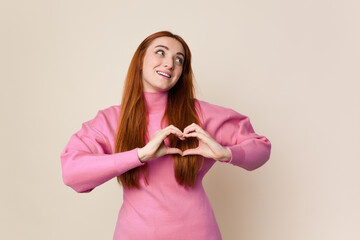 Young red hair woman isolated smiling and showing a heart shape with hands.