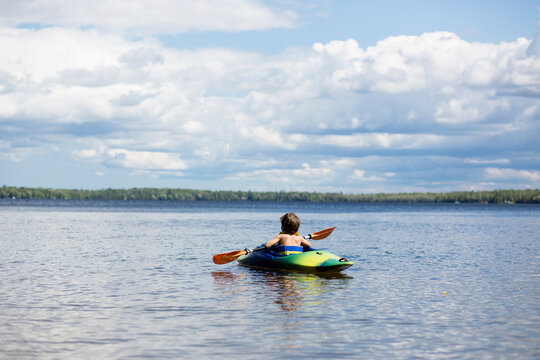 Rear view of boy kayaking in lake against cloudy sky