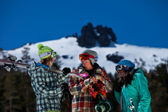 Three Friends (one Male And Two Females) Hanging Out With Skis And A Snowboard In Front Of A Ski Resort.