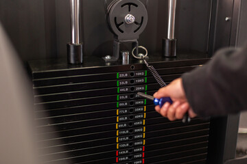 Crop young athlete choosing the weight on the gym machine 