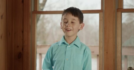 A Latino boy laughs uncrontrollably at something or someone.
