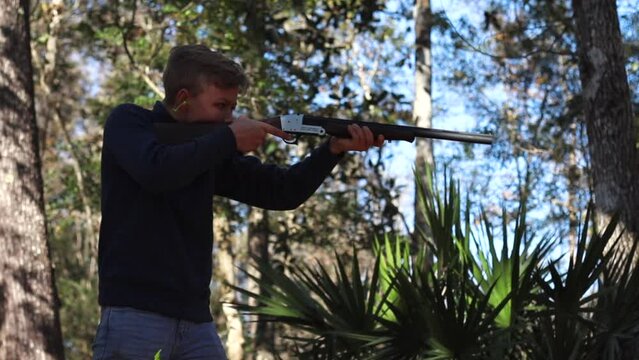 Young boy aims gun at target. Young man aims a rifle while hunting for wild animals. Boy getting ready to shoot a powerful shotgun.
